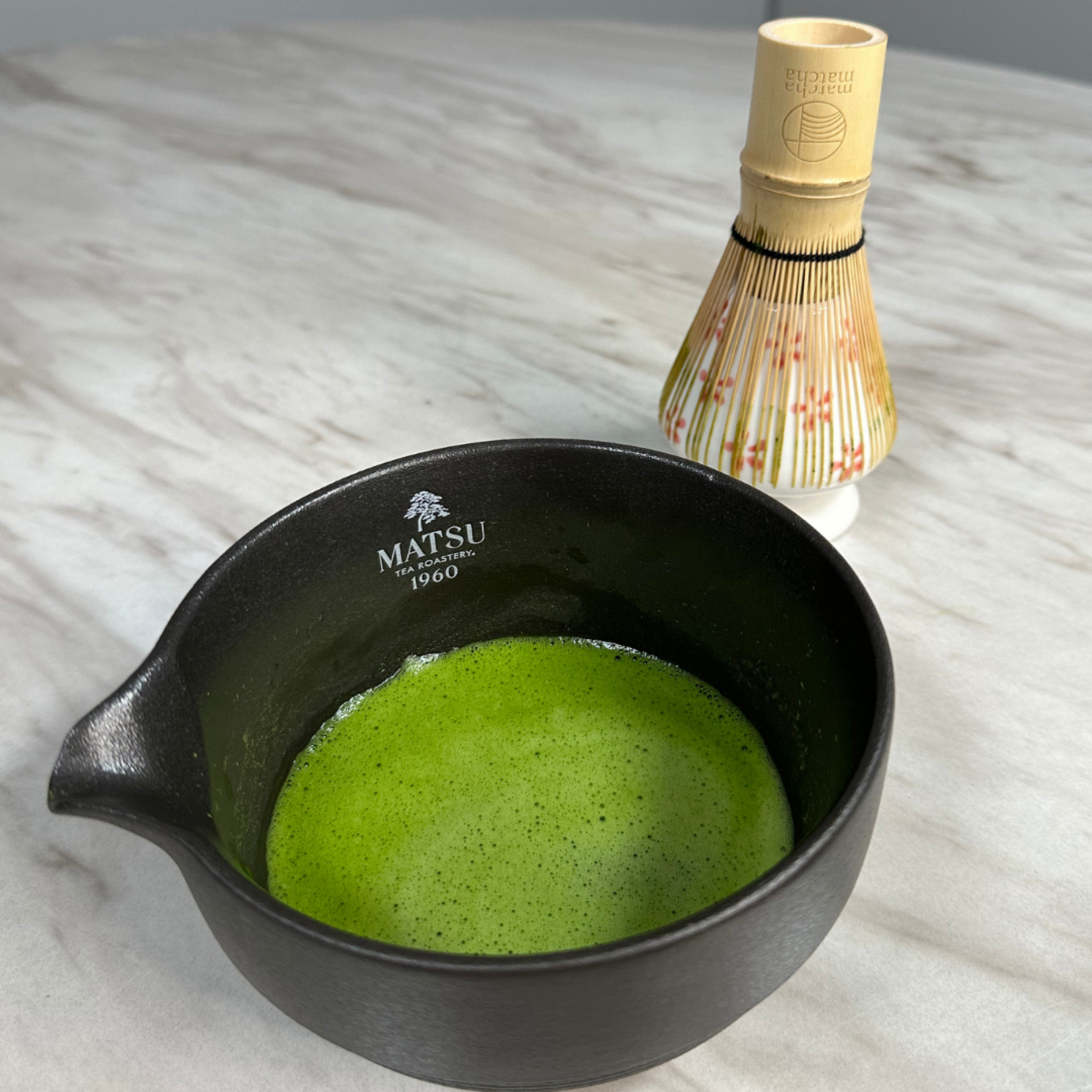 bamboo chasen whisk with matcha in a black bowl on a marble surface